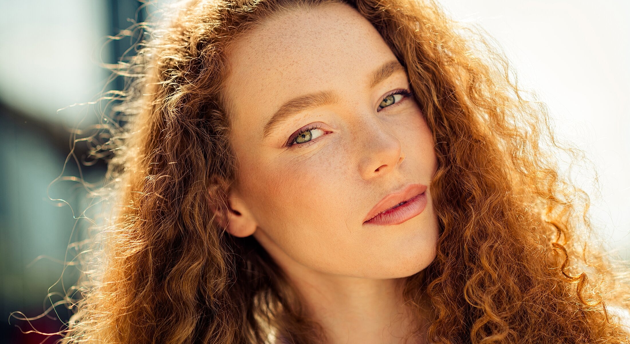 Woman with curly hair and freckles outdoors.