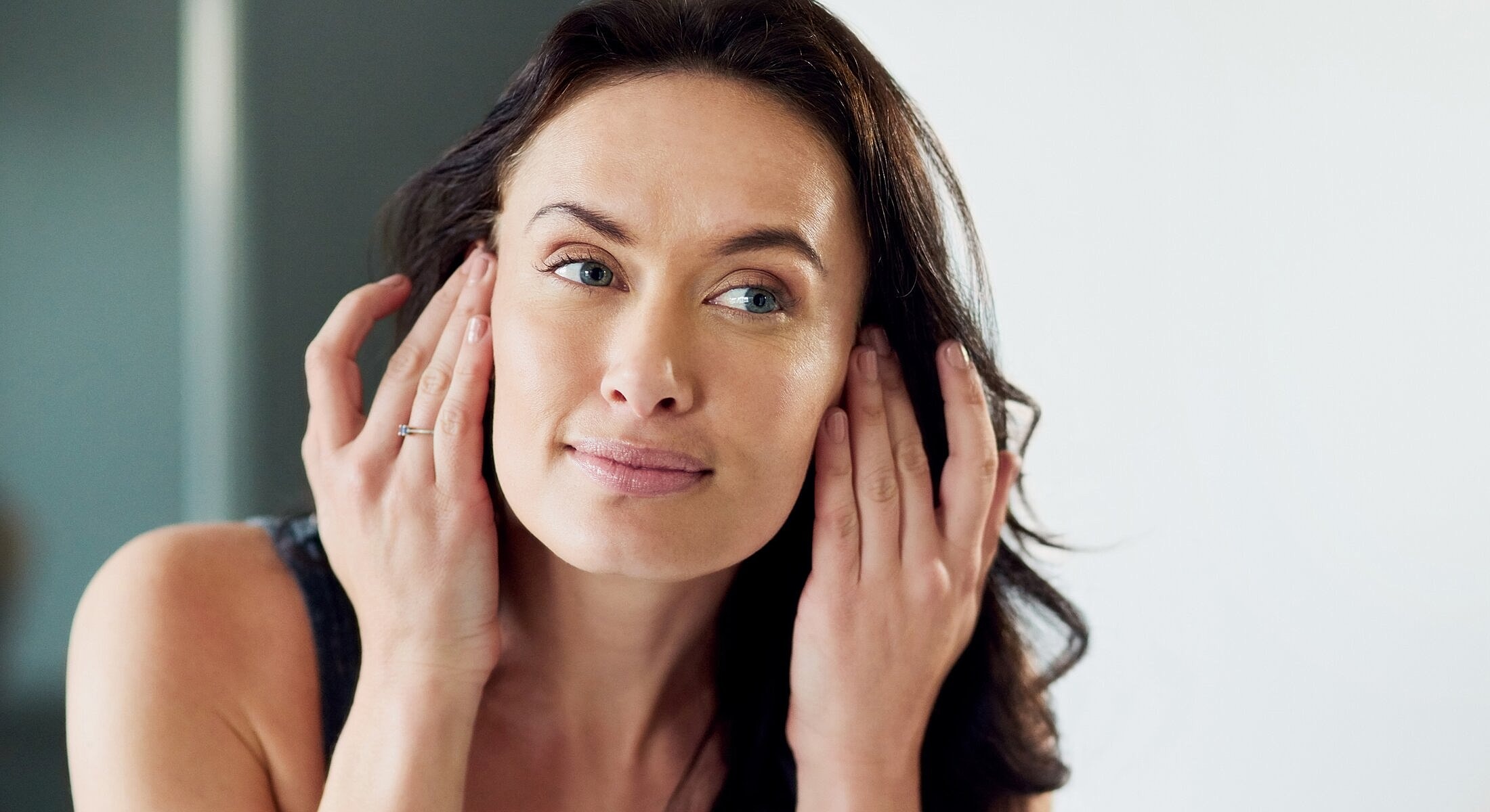 Woman gently touching her face in mirror.